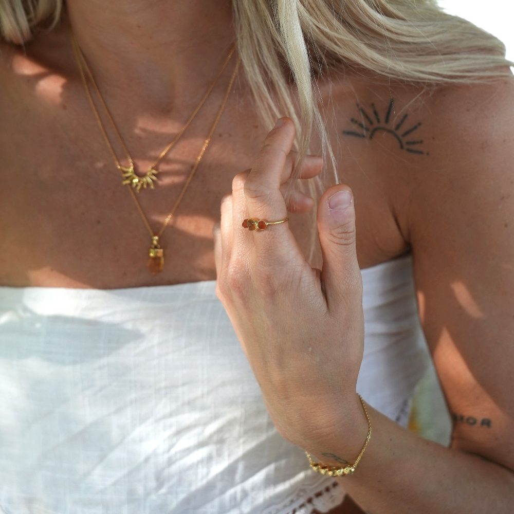 Vackra smycken med råa kristaller burna av blond kvinna med sol tatuering. Guldsmycken med råa kristaller som ring, halsband och armband.