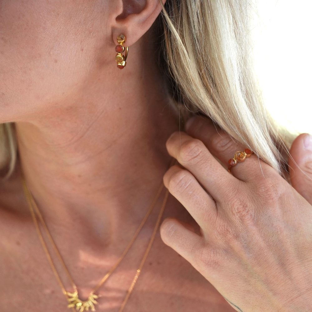 Blond kvinna bär smycken med råa kristaller i guld. Örhängen i guld med råa kristaller.