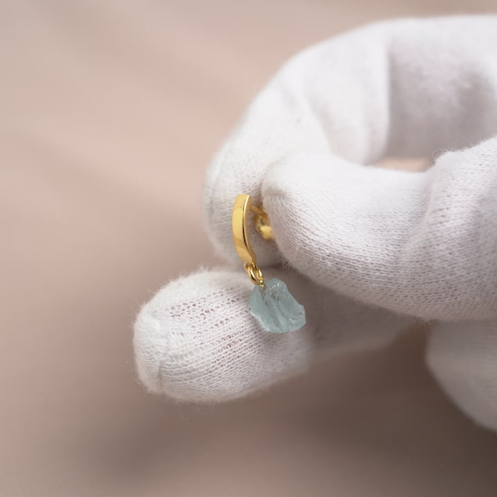 Guldörhängen med en rå blå kristall. Örhängen i guld med en blå kristall Akvamarin i en rå form.